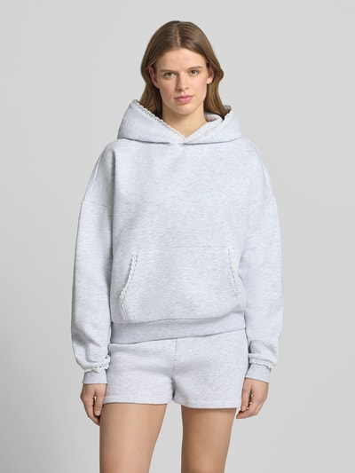 Frauenmodel trägt Hoodie mit Spitzenkanten an Kapuze, Känguru-Tasche und Ärmelbund von Review, Material-Mix mit Baumwoll-Anteil, Relaxed-Fit, Label-Stitching, hellgrau, Ganzkörperansicht von vorne.