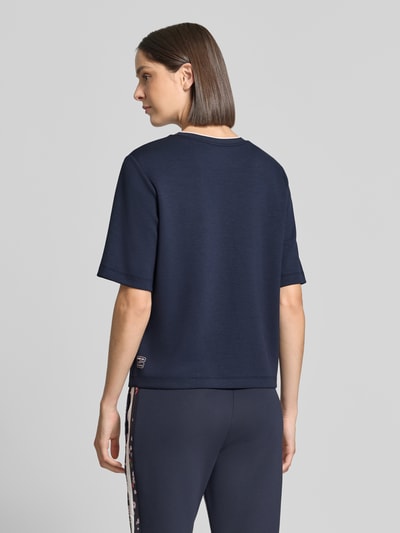 Modelka prezentuje Relaxed Fit T-Shirt aus Viskose-Mix von Marc Cain w kolorze granatowym, detal z logo, okrągły dekolt, damski t-shirt z mieszanki wiskozy, długość tyłu w rozmiarze 36: 54 cm, widok całej sylwetki z tyłu.