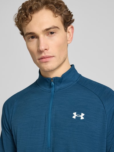 Männermodel trägt Sweatshirt mit kurzem Reißverschluss und Logo-Print von Under Armour in Blau, Struktur-Oberfläche, Nahaufnahme Oberkörper. Rückenlänge 74 cm, Ärmellänge 64 cm, Gerader-Schnitt, Stehkragen, Größe M.