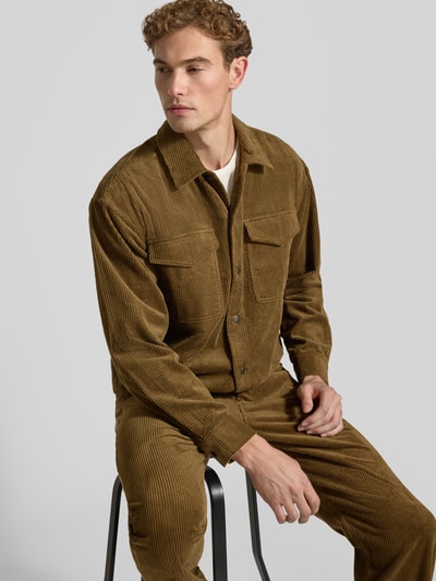 Männermodel trägt Regular Fit Hemdjacke aus Cord Modell 'David' von Wood Wood in Braun, fein gerippte Textur, Nahaufnahme Oberkörper. Herren Hemdjacke aus reiner Baumwolle, Kentkragen, Brusttaschen, Rückenlänge bei Größe M 73 cm.