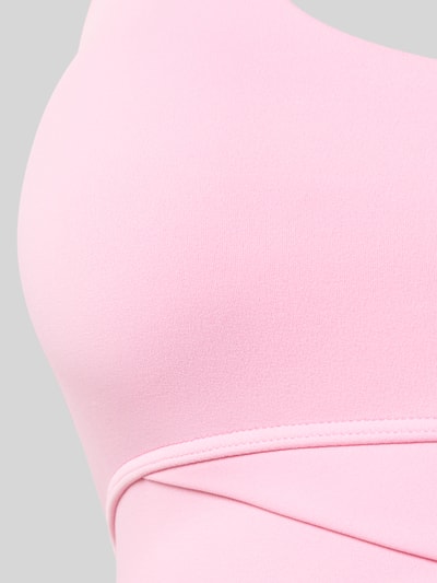 Frauenmodel trägt Sport-BH mit Neckholder Modell 'ACTIVE' von P.E Nation in Rosa, glatte Textur, Detailaufnahme Oberkörper.