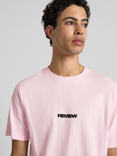 Męski model nosi t-shirt mit Logo und Rundhalsausschnitt von REVIEW, bawełna, krój relaxed fit, logo, okrągły dekolt, długość tyłu 68 cm w rozmiarze M, zbliżenie na górę ciała.
