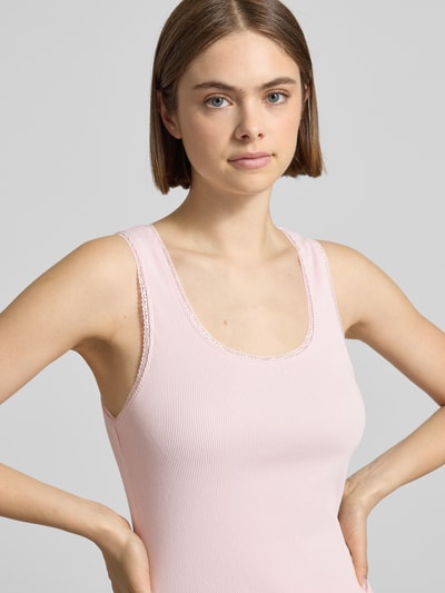Frauenmodel trägt Tanktop in Ripp-Optik Modell 'Jolie' von OH APRIL aus Baumwoll-Elasthan-Mix mit Spitzenbesatz, Rundhalsausschnitt, Slim-Fit, sanft rosafarbene Struktur, feine Linien, Nahaufnahme Oberkörper.