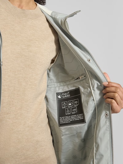 Frauenmodel trägt Jacke mit Ärmelriegeln von NAUTGÅRD in hellem Grau, glatte Textur, Reißverschlusstaschen, Detailaufnahme Innenansicht. Regular Fit, Kapuze mit Tunnelzug, Knopfleiste, Rückenlänge 90 cm, Schulterbreite 45 cm, Brustweite 51 cm, Ärmellänge 62 cm.