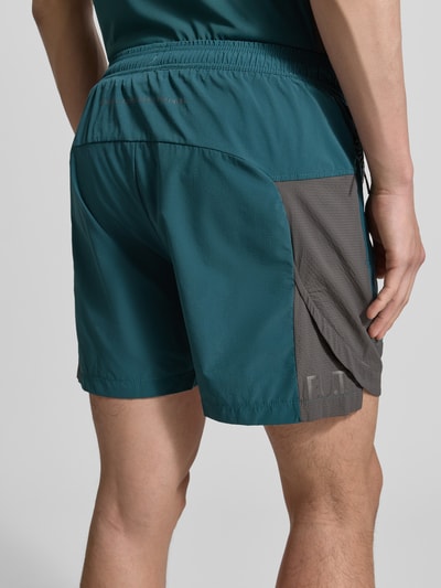 Männermodel trägt Shorts mit Reißverschlusstaschen Modell 'HALO DIVISION' von HALO in Türkis und Grau, Regular-Fit, elastischer Bund, Ganzkörperansicht Rückansicht. Kontext: Herren Shorts, Bundweite 40 cm, Innenbeinlänge 10 cm, Größe M.
