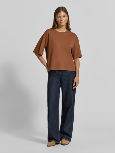 Frauenmodel trägt Oversized T-Shirt aus reiner Baumwolle von s.Oliver RED LABEL in Braun, kombiniert mit dunkler Jeans, Ganzkörperansicht von vorne.