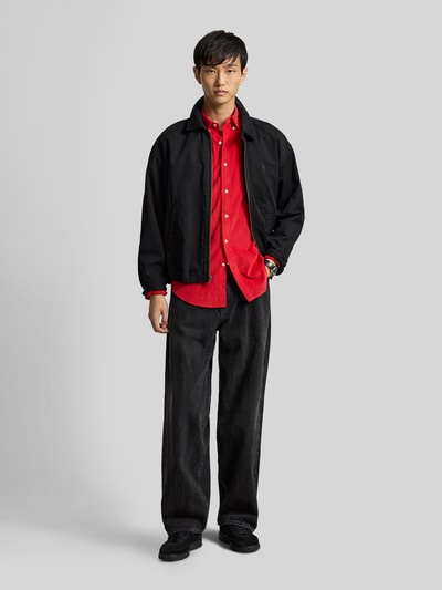 Männermodel trägt Custom Fit Freizeithemd aus reiner Baumwolle von Polo Ralph Lauren in Rot, dazu schwarze Hose und Jacke, Ganzkörperansicht von vorne.