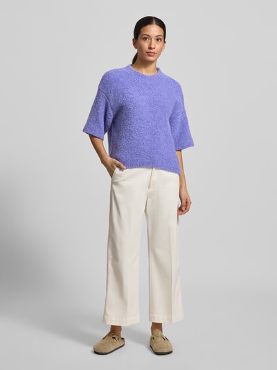 Modelka nosi Strickpullover mit gerippten Abschlüssen Modell 'ZOLLY' od American Vintage, luźny krój, fioletowy melanż, półrękaw, faktura dzianiny, widok całej sylwetki z przodu.