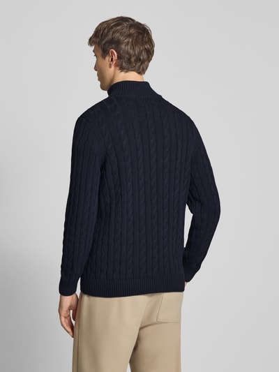 Männermodel trägt Strickpullover aus reiner Baumwolle von Superdry, dunkelblau, Zopfmuster, eng anliegend, Ganzkörperansicht Rückansicht.