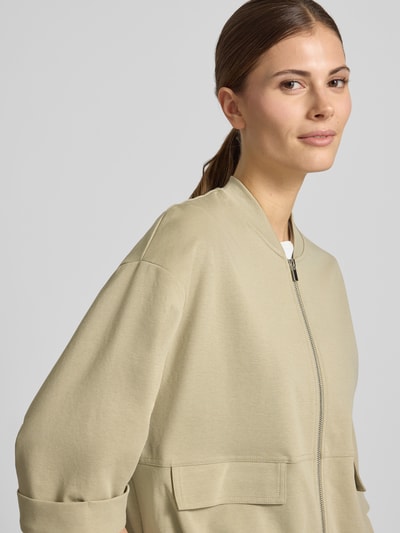 Vrouwenmodel draagt Blouson mit Reißverschluss und Pattentaschen Modell 'Goros' van OPUS, beige, katoenmix met stretch, relaxed fit, staande kraag, 3/4-mouw, detailopname bovenlichaam.