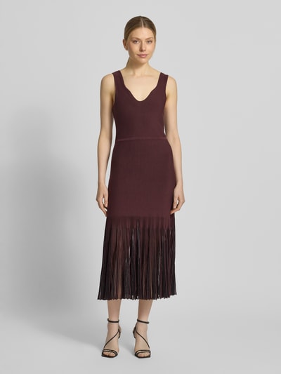 Modelka kobieca nosi Strickkleid aus Rippstrick od BOSS, kolor bordowy, prążkowana faktura, dekolt V, bez rękawów, przezroczyste plisowane falbany, długość do kolan, krój slim fit, widok całej sylwetki z przodu.