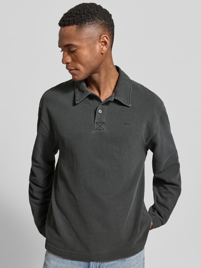 Męski model nosi Loose Fit Poloshirt aus Baumwolle Modell 'Thiago' od Wood Wood, ciemnoszary kolor, mięsista bawełna, polokołnierzyk, label-stitching, długość tyłu w rozmiarze M: 71 cm, Ganzkörperansicht z przodu.