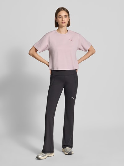 Frauenmodel trägt Relaxed Fit T-Shirt aus Häkelspitze von PUMA in zartem Rosa, schwarze Hose, neutrale Farben, Ganzkörperansicht von vorne, Damen T-Shirt von PUMA.