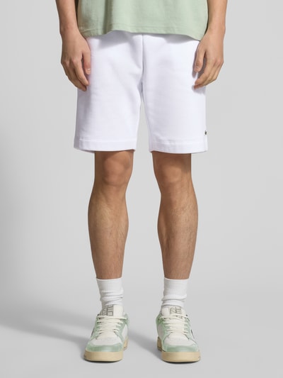Mężczyzna nosi Regular Fit Sweatshorts aus Baumwoll-Mix von Lacoste, białe, gładkie, z elastycznym pasem i kieszeniami, Ganzkörperansicht von vorne.