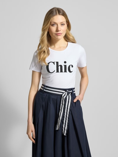 Frauenmodel trägt T-Shirt mit Rundhalsausschnitt und Perlen von More & More, Weiß mit Statement-Print, regular Fit, Nahaufnahme Oberkörper.