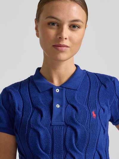Kobiece modelka nosi koszulkę polo z wyhaftowanym logo Poloshirt mit Label-Stitching od Polo Ralph Lauren z bawełny, krój regular fit, kołnierzyk polo, krótka listwa guzikowa, kolor niebieski, tekstura dzianiny, długość tyłu 55 cm przy rozmiarze S, zbliżenie na górną część ciała.