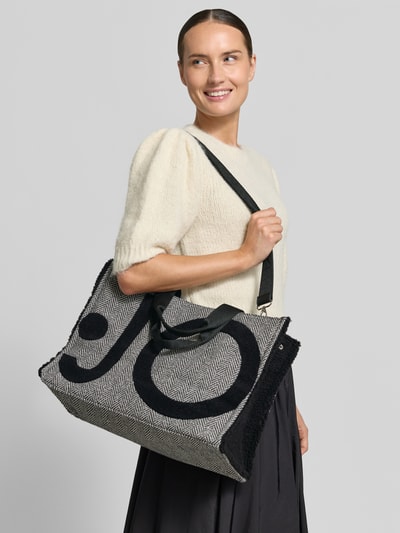 Kobiece modelka nosi Torebkę Tote Bag mit Label-Details od Liu Jo White w odcieniach czerni i bieli, Główna przegroda z zamkiem błyskawicznym, odpinany pasek na ramię, krótkie uchwyty, detal z logo, przegródka wewnętrzna zapinana na zamek błyskawiczny, Szerokość w rozmiarze 1: 42 cm, Długość w rozmiarze 1: 30 cm, Głębokość w rozmiarze 1: 20 cm, Długość paska na ramię w rozmiarze 1: 42 cm, widok całej sylwetki z przodu