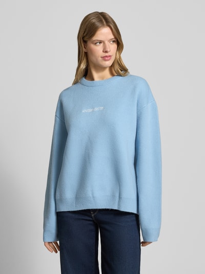 Frauenmodel trägt Oversized Strickpullover mit Rückenmotiv von ANOTHER COTTON LAB, hellblau, Rundhalsausschnitt, Label-Stitching, Damen, Ganzkörperansicht von vorne.