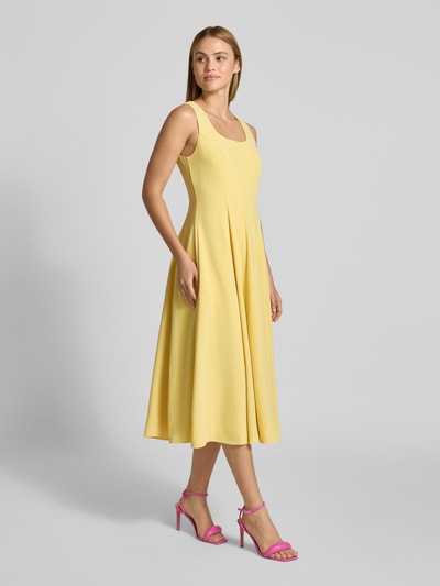 Frauenmodel trägt gelbes A-Linien Midikleid mit Rundhalsausschnitt Modell 'ARLOTT' von Ted Baker, breite Träger, Reißverschluss hinten, Ganzkörperansicht von vorne.