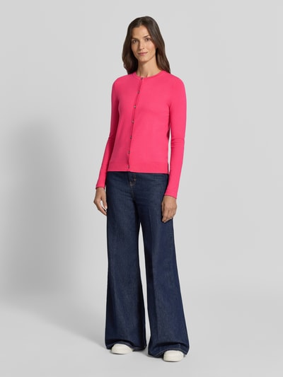 Vrouwenmodel draagt Regular Fit gebreid jack uit Viscosemix met geschulpte zoom van Christian Berg Woman, lange mouw, knoopsluiting, ribboorden, ruglengte bij maat S 56 cm, mouwlengte bij maat S 61 cm, felroze kleur, ronde vormen, glad breisel, Ganzkörperansicht van voren.