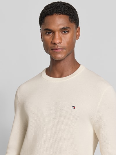 Męski model nosi Regular Fit Pullover aus reiner Baumwolle von Tommy Hilfiger w kolorze kremowym, subtelna tekstura, nahaufnahme górnej części ciała.