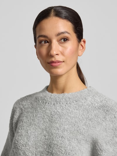Modelka prezentuje Strickpullover mit gerippten Abschlüssen Modell 'ZOLLY' od American Vintage, jasnoszara faktura, półokrągły dekolt, luźny krój, miks wełny z alpaką, długość pleców 60 cm, długość rękawa 33 cm, zbliżenie górnej części ciała.