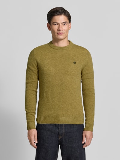 Männermodel trägt Slim Fit Strickpullover aus reiner Wolle mit Label-Stitching von MCNEAL, olivgrün, gerippte Abschlüsse, Ganzkörperansicht von vorne.