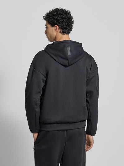 Männermodel trägt schwarze Sweatjacke mit Kapuze von adidas Sportswear, Regular Fit, Label-Print, Material-Mix, Ganzkörperansicht Rückansicht.