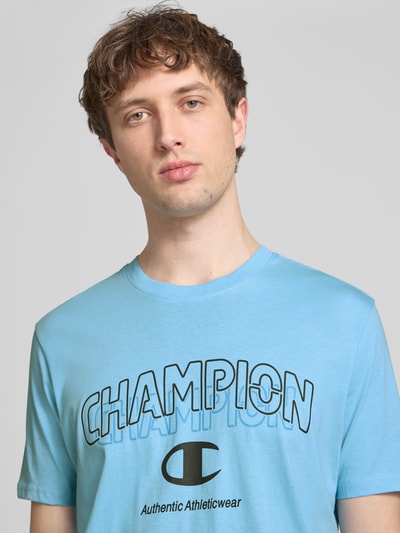 Männermodel trägt T-Shirt mit Label-Print und Rundhalsausschnitt von CHAMPION in Blau, Reine Baumwolle, Regular-Fit, Nahaufnahme Oberkörper.