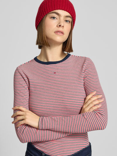 Vrouwenmodel draagt Slim Fit Langarmshirt uit katoenmix van Tommy Jeans, gestreept meerkleurig fijnrib, logo detail, close-up bovenlichaam.