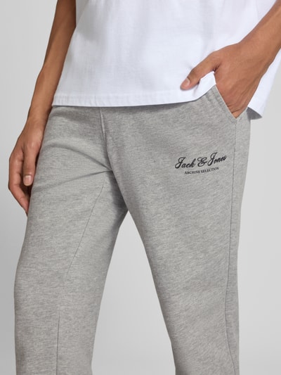 Männermodel trägt sweatpants met labelprint Model 'GORDON' van JACK & JONES in lichtgrijs, steekzakken, los model, tunnelkoord, detailopname rechterbeen
