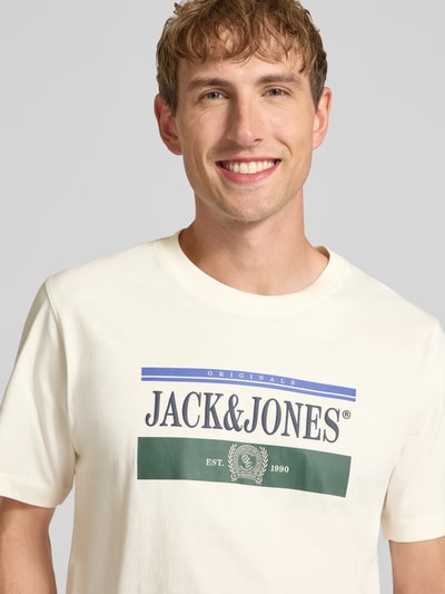 Męski model nosi t-shirt z nadrukiem z logo, Model 'FREDERIKSBERG' od JACK & JONES, bawełna, prosty krój, okrągły dekolt, długość tyłu w rozmiarze M: 70 cm, zbliżenie na górną część ciała.