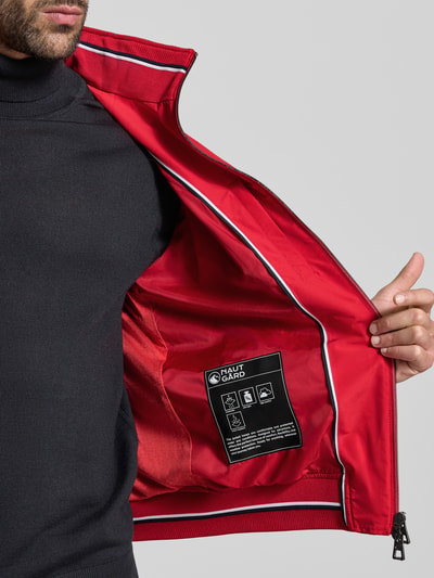 Männermodel trägt Regular Fit Jacke mit Kapuze Modell 'Como' von NAUTGÅRD in Rot, Innenansicht, Nahaufnahme Oberkörper, glatte Textur, Kontext: Stehkragen, Zweiwegereißverschluss, Eingrifftaschen, elastische Abschlüsse.