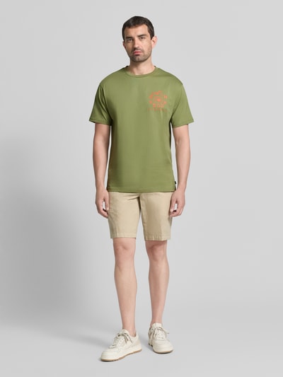 Männermodel trägt T-Shirt mit Label-Print und Rundhalsausschnitt van Scotch & Soda in kaki, puur katoen, regular fit, ruglengte maat M 72 cm, ganzlichaamsvooraanzicht.