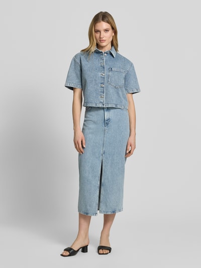 Frauenmodel trägt figurbetonten Jeansrock aus reiner Baumwolle Modell 'GATJE' von HUGO in Denim-Optik mit Strukturmuster, Maxi-Länge, Label-Patch, 5-Pocket-Design und Frontschlitz, Ganzkörperansicht von vorne.
