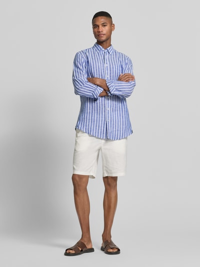 Mężczyzna model nosi Slim Fit Freizeithemd aus reinen Leinen od Christian Berg Men, niebiesko-białe pionowe paski, kołnierzyk typu button down, listwa guzikowa, krój slim fit, czysta tkanina lniana, długie rękawy, sportowe mankiety, długość tyłu w rozmiarze M: 79 cm, szerokość w rozmiarze M: 48 cm, długość rękawów w rozmiarze M: 65 cm, długa koszula, widok całej sylwetki z przodu