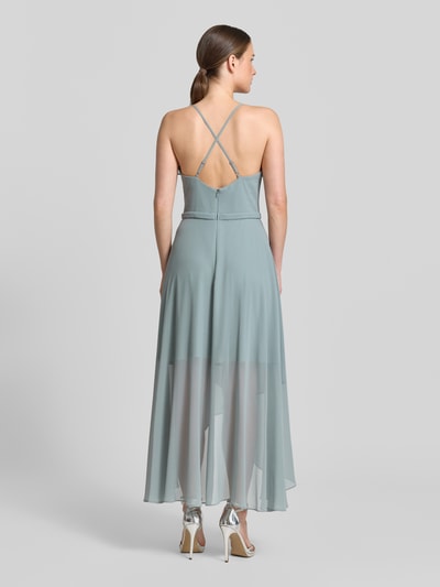 Frauenmodel trägt Cocktailkleid aus Chiffon mit Volants von V.M. in Hellgrün, A-Linie, V-Ausschnitt, transparenter Midirock, Ganzkörperansicht Rückansicht.