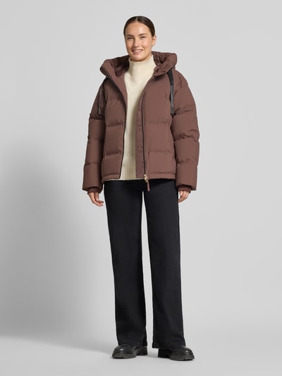 Modelka nosi kurtkę z efektem pikowania od MOS MOSH, Model 'Jilly Hope', krój regular fit, kaptur z tunelem, wpuszczane kieszenie, długość tyłu w rozmiarze S: 63 cm, szerokość ramion w rozmiarze S: 50 cm, szerokość klatki piersiowej w rozmiarze S: 58 cm, długość rękawów w rozmiarze S: 64 cm, zamek błyskawiczny. Kolory: brązowy, czarny, kremowy. Widok całej sylwetki z przodu.