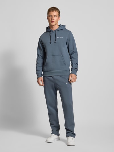 Męski model nosi Straight Fit Sweatpants mit Label-Stitching od CHAMPION, kolor niebieski, mieszanka bawełny, elastyczny pas, wyhaftowane logo, długość wewnętrzna nogawki 70 cm, widok całej sylwetki z przodu.