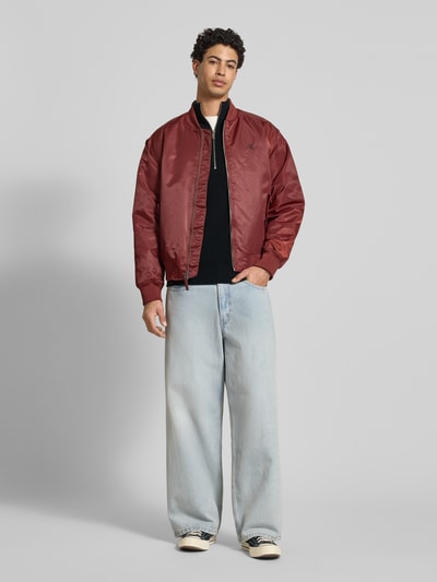 Männermodel trägt Loose Fit Troyer mit gerippten Abschlüssen von Calvin Klein Jeans, schwarz, mit kurzem Reißverschluss, Ganzkörperansicht von vorne.