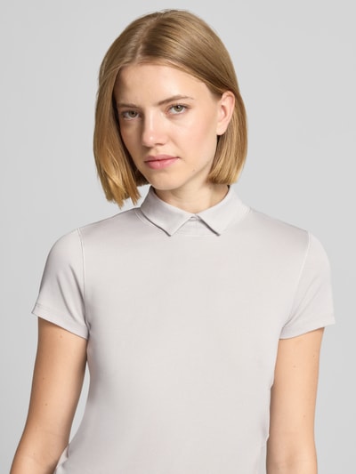Frauenmodel trägt Slim Fit T-Shirt mit hochschließendem Polokragen von Marc Cain aus Baumwoll-Elasthan-Mix in Hellgrau, Nahaufnahme Oberkörper.