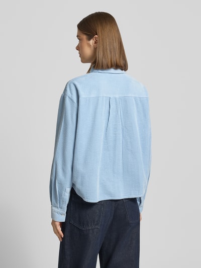 Vrouwenmodel draagt Relaxed Fit Hemdbluse aus reiner Baumwolle van Marc O'Polo Denim in effen lichtblauw corduroy met borstzak, afgeronde rompzoom, overhemdkraag en labelstitching, rugpas met plooien, lange mouw met manchet, rugaanzicht, ganzekijk.