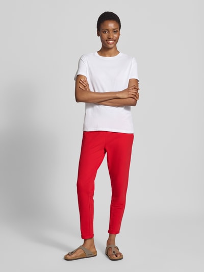 Kobiece model prezentuje spodnie dresowe Slim Fit Sweatpants aus Baumwoll-Mix Model 'Cozy Nights' od Mey, krój slim fit, mieszanka bawełny, elastyczny pas z tunelem, wpuszczane kieszenie, skrócony krój, kolor czerwony, tło jasnoszare, Ganzkörperansicht von vorne.
