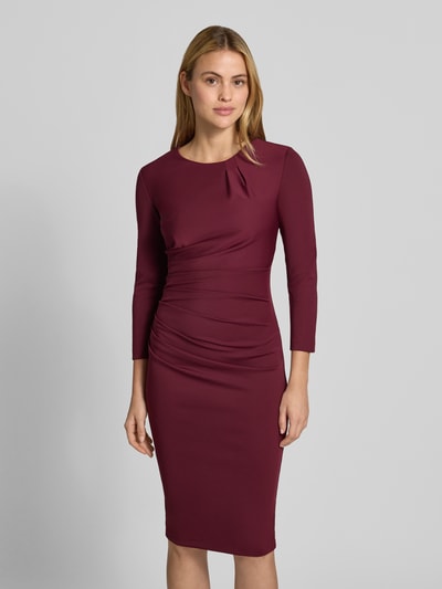 Frauenmodel trägt Cocktailkleid mit Raffungen von Rinascimento in Bordeaux, Langarm, knieumspielend, Material-Mix, Ganzkörperansicht von vorne.