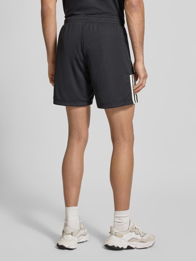 Männermodel trägt Regular Fit Shorts mit Logo-Print Modell 'Tiro' von adidas Sportswear, elastischer Bund, schwarze Textur, Ganzkörperansicht Rückansicht. Bundweite 36 cm, Innenbeinlänge 18 cm, Größe M.