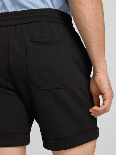 Männermodel trägt Regular Fit Shorts mit Viskose-Anteil Modell 'NEWKODYL' von Only & Sons in Schwarz, Melange-Optik, Nadelstreifenmuster, Gesäßtasche, fixierter Beinumschlag, elastischer Bund, Nahaufnahme Rückansicht.