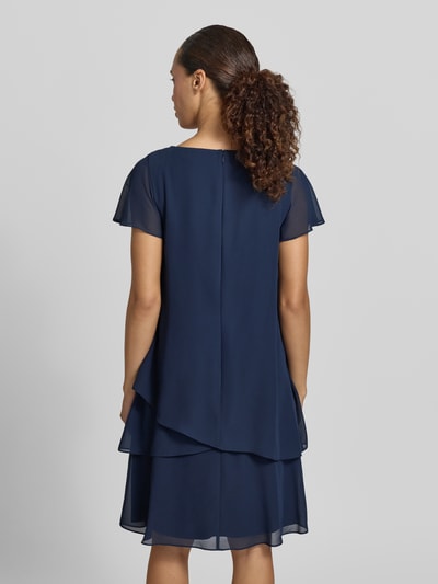 Frauenmodel trägt knielanges Cocktailkleid mit Schlüsselloch-Ausschnitt von Christian Berg Cocktail aus dunkelblauem Chiffon, Stufen-Look, Perlen, Gerader-Schnitt, Rückenlänge 93 cm, Brustweite 47 cm, Ärmellänge 12 cm, Ganzkörperansicht Rückansicht.