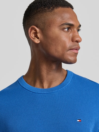 Mannelijk model draagt Regular Fit Gebreide pullover uit puur katoen van Tommy Hilfiger, effen kleuren, gebreide look, logodetail, ronde hals, lange mouw, geribde mouwboord en rompzoom, knitwearverwerking, Nahaufnahme bovenlichaam.