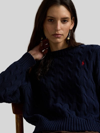 Kobiece model nosi Regular Fit Strickpullover aus reiner Baumwolle od Polo Ralph Lauren, granatowy, wzór warkoczowy, logo, krój regular fit, dzianina, bawełna, crew neck, długie rękawy, ściągacze; zbliżenie na górną część ciała.