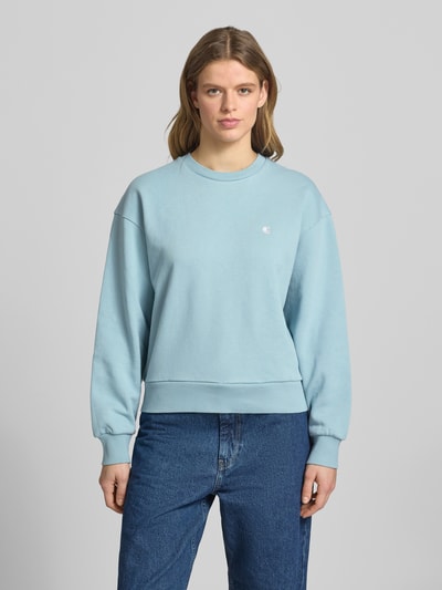 Frauenmodel trägt Sweatshirt mit Logo-Stitching Modell 'CASEY' von Carhartt Work In Progress aus Reine Baumwolle, Loose-Fit, Rundhalsausschnitt, überschnittene Schultern, hellblaue Farbe, glatte Textur, Ganzkörperansicht von vorne.